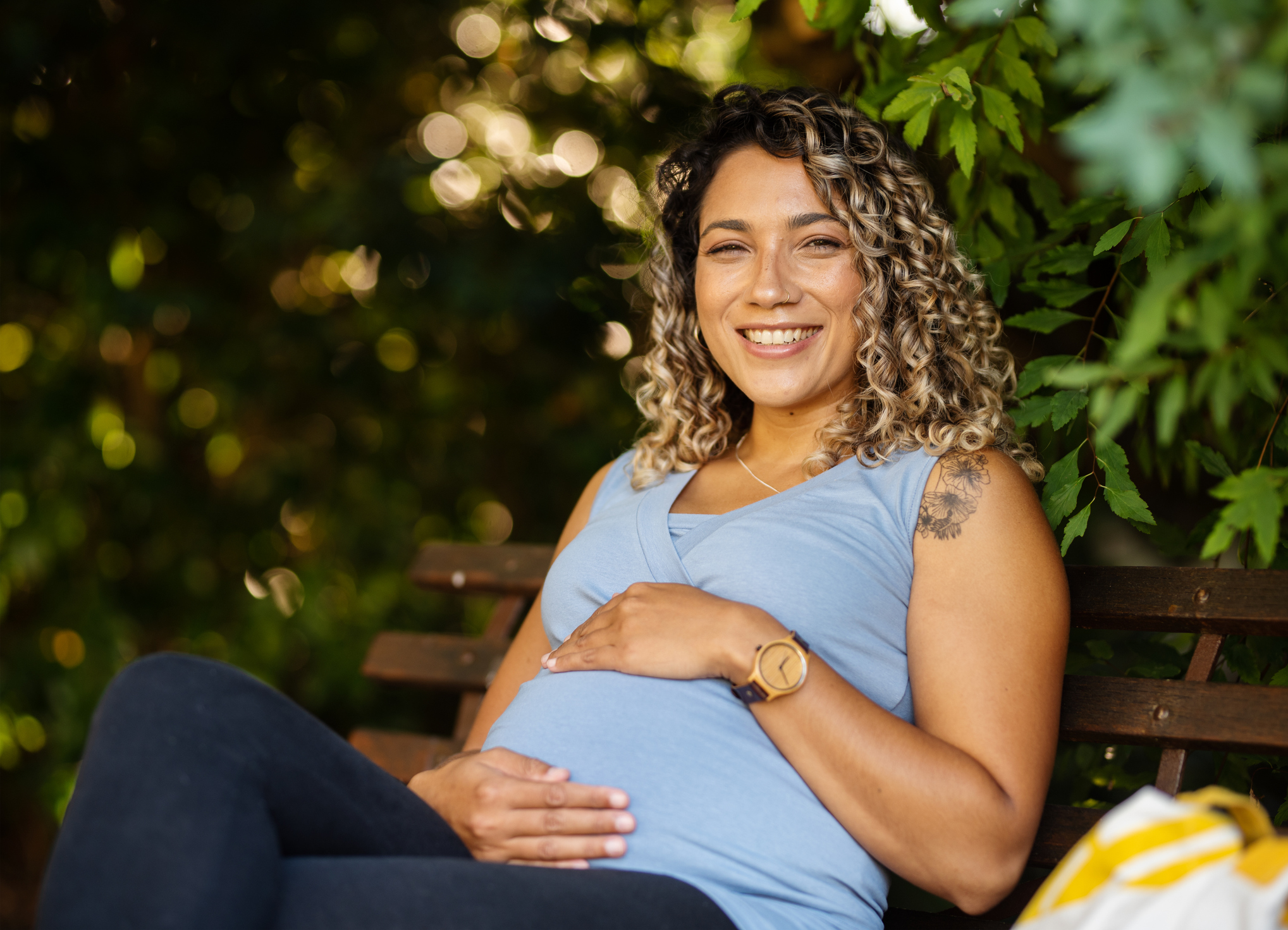Portrait of a smiling young pregnant woman cradling her tummy while sitting outside on a park bench in the summer